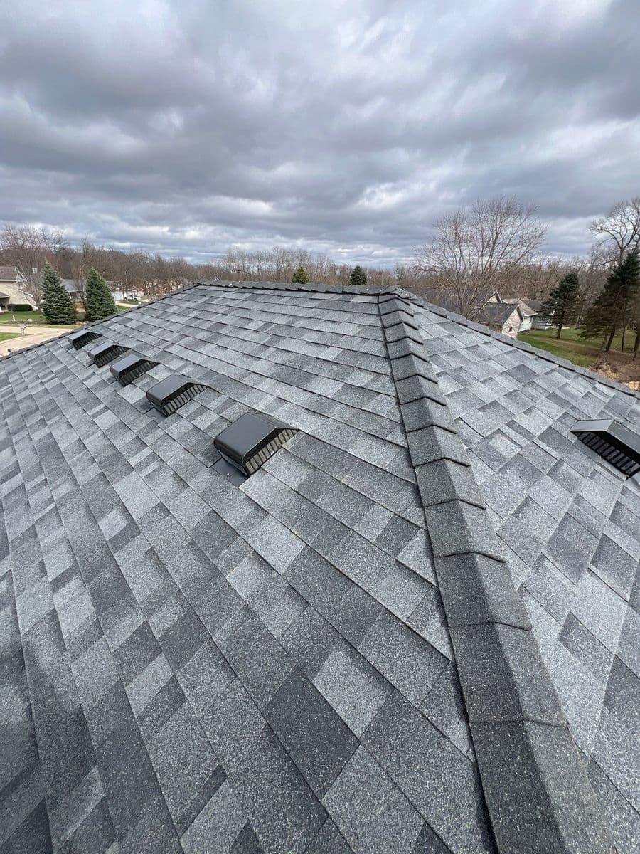 Aerial view of a gray shingle roof with skylights under a cloudy sky.