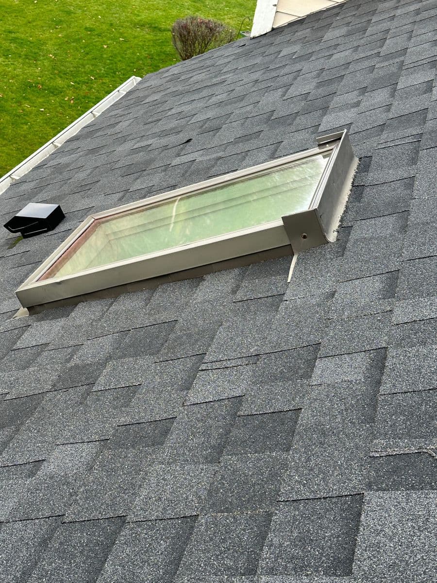 Skylight on a sloped roof with grey shingles and green lawn in the background.