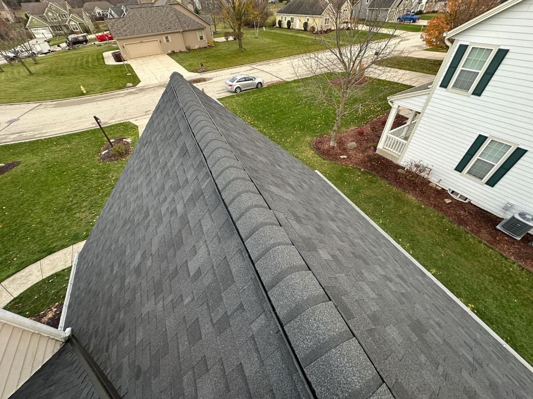 Aerial view of a gray asphalt shingle roof on a suburban home with green lawns and driveways.