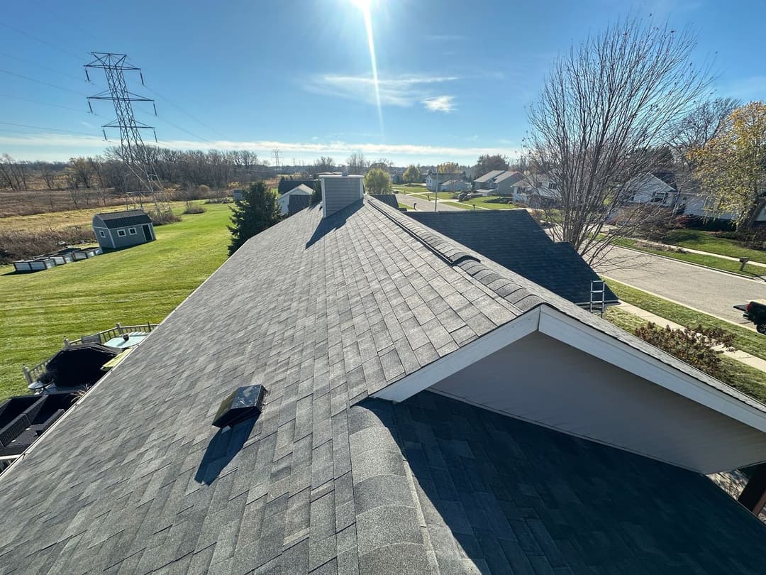View of a residential roof with shingle roofing and clear blue sky in the background.