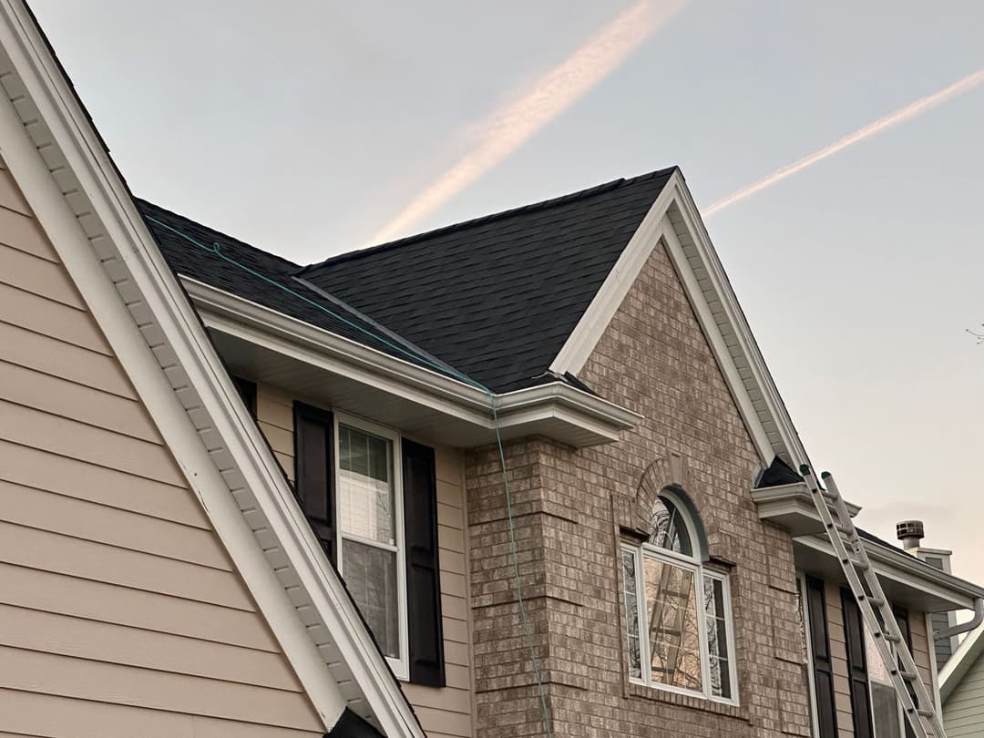 Roof repair on a two-story house with brick and siding, featuring a ladder and clear sky.
