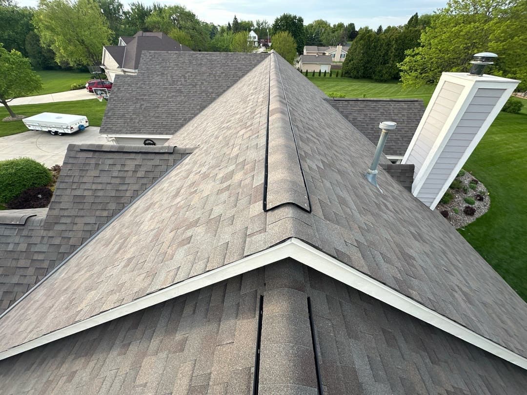 Aerial view of a residential roof with shingles, chimneys, and surrounding greenery.