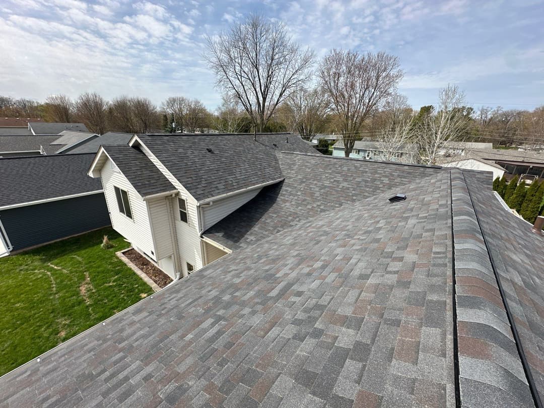 Aerial view of a residential roof with asphalt shingles and surrounding green lawn.
