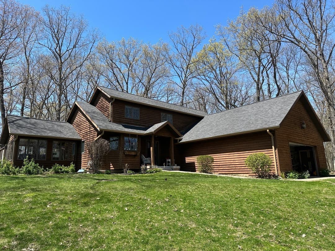 Modern wooden house surrounded by trees on a sunny day, showcasing a spacious yard.