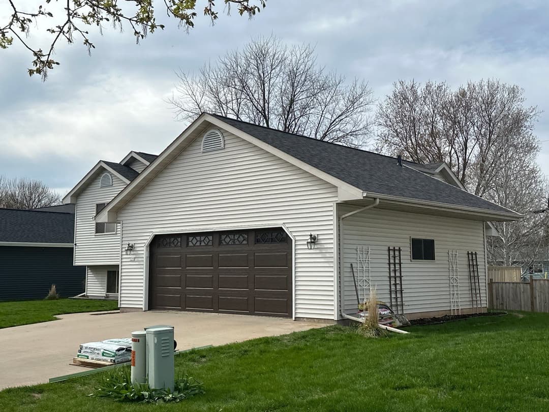Side view of a modern white house with a brown garage door and landscaped yard.