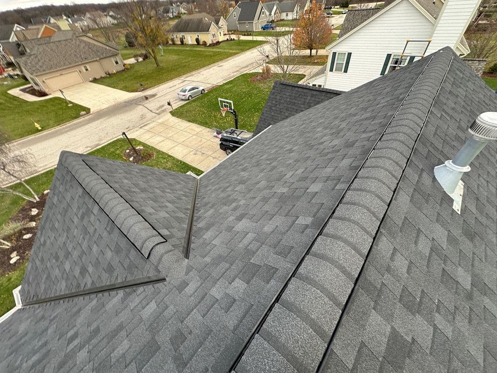 Aerial view of a gray shingled roof with suburban homes in the background.